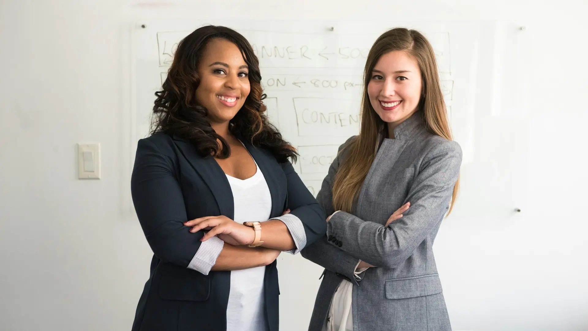 two women in suits standing beside wall